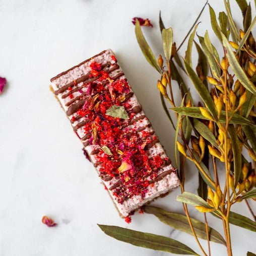 A tray of Charlies Rawsome Vegan Berry Ripe Raw Slices, featuring bright pink berry layers and a dark chocolate base.